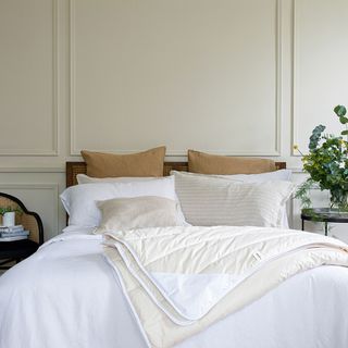 Bed with white bed linen against a beige panelled wall