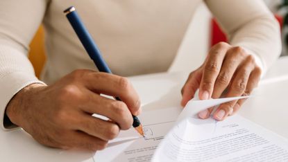 A man signs a document, only his hands showing.
