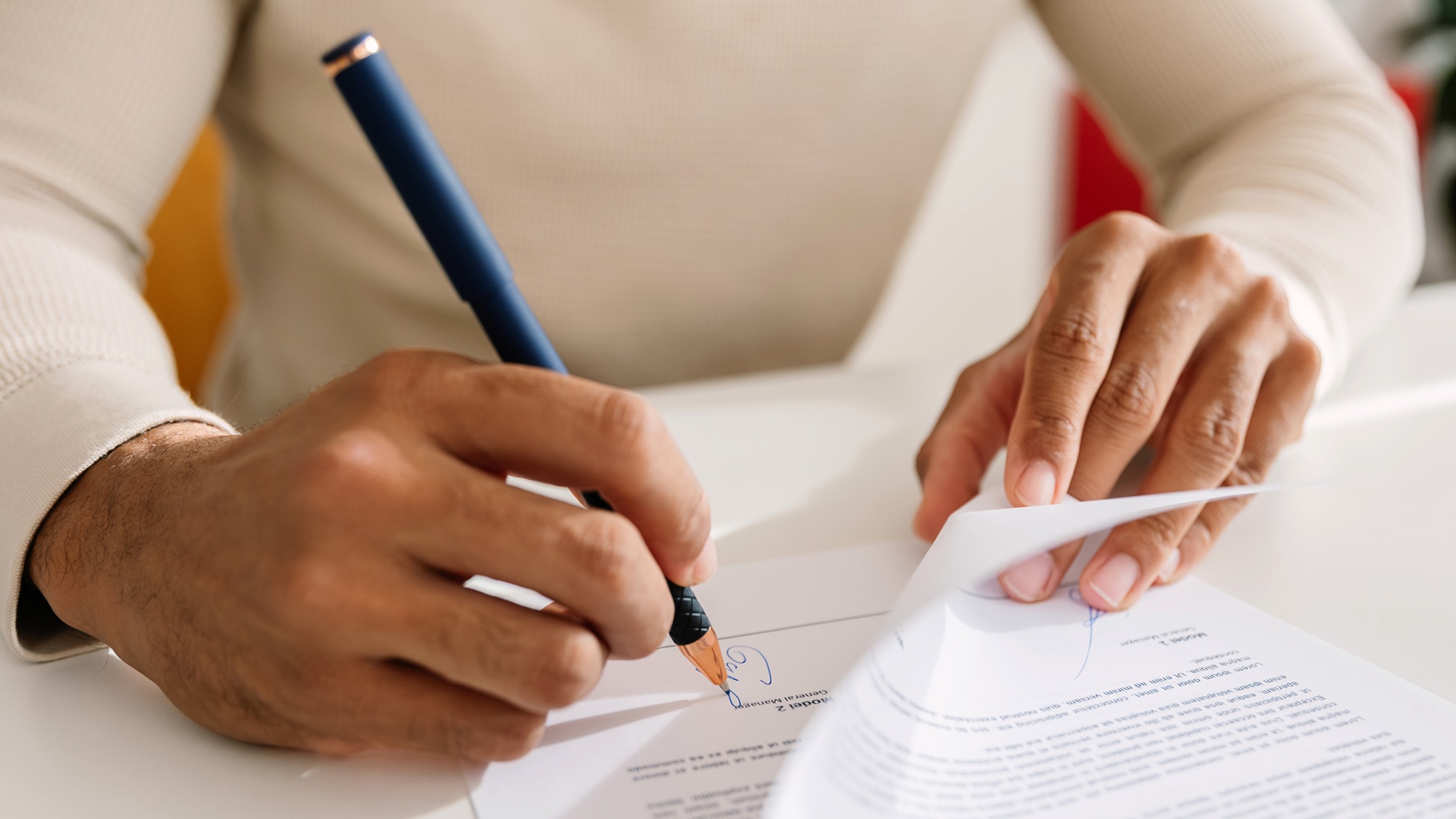 A man signs a document, only his hands showing.