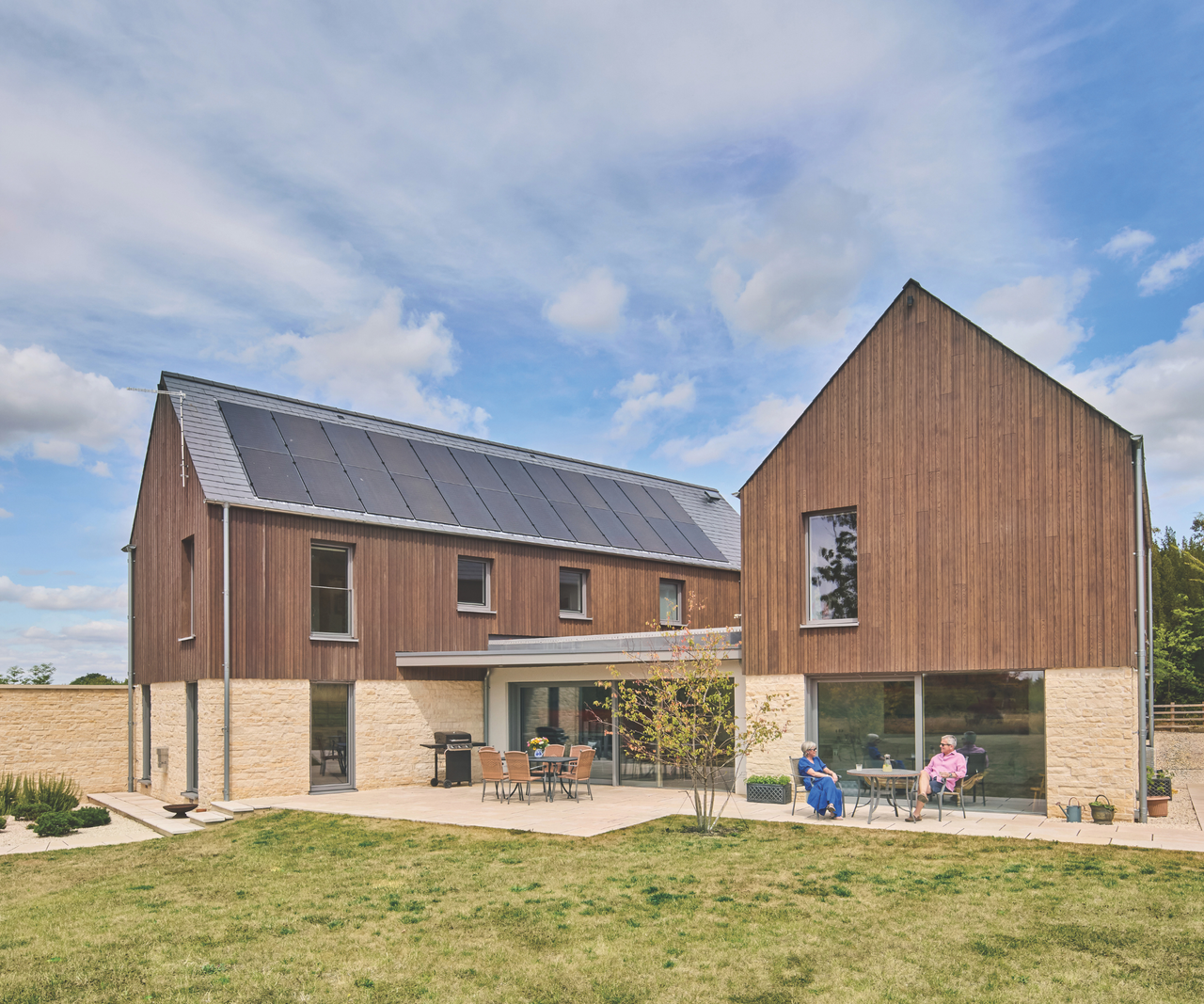 exterior of wood-cladded house with couple sitting at patio in garden