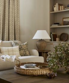 Close up of living room seating area with wooden coffee table, decorated with ornaments and vase of flowers, lampshade and shelving in background