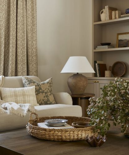 Close up of living room seating area with wooden coffee table, decorated with ornaments and vase of flowers, lampshade and shelving in background