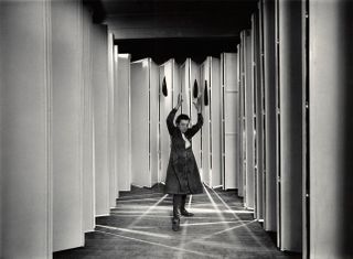 A blakc and white photo of Louise Bourgeois with her hands in the air.