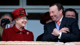 Queen Elizabeth wearing a red hat and coat smiling at horse trainer Nicky Henderson at the 2009 Cheltenham Festival