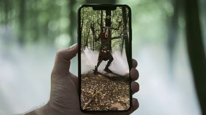 A hand holds a phone showing an augmented reality monster
