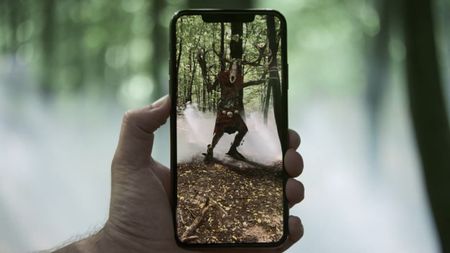 A hand holds a phone showing an augmented reality monster