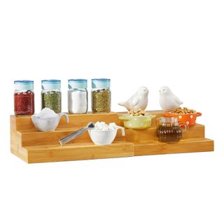 A wooden tiered countertop shelf with spices, sugar, and bird decorations on it