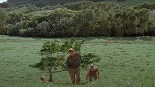 A man and two children walking up a green hill in Jurassic Park