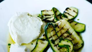 ribbons of grilled zucchini strewn across a plate alongside a ball of fresh mozzarella