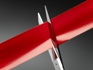 A pair of scissors cutting red tape