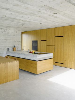 Oak wooden accents for cupboards, furniture and windows soften the grey concrete walls