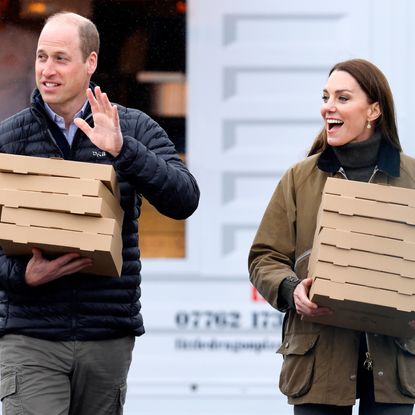 Prince William and Princess Kate smiling and carrying pizza boxes