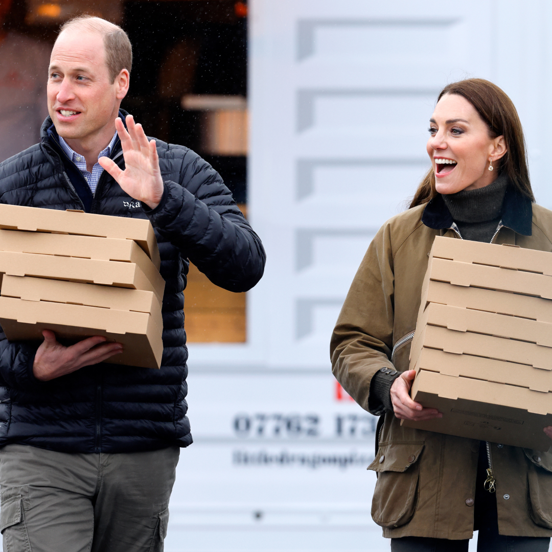 Prince William and Princess Kate smiling and carrying pizza boxes
