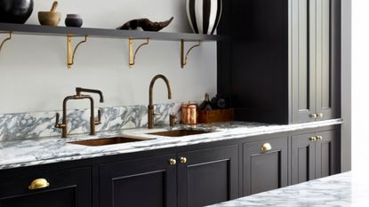 A kitchen with black cabinets, and a brass sink and tap