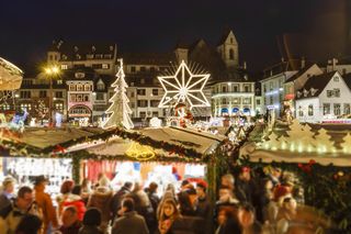 Star and Christmas tree lights are turned on at night above Christmas market stalls in Basel, Switzerland