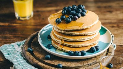 A stack of pancakes on a plate topped with blueberries and syrup