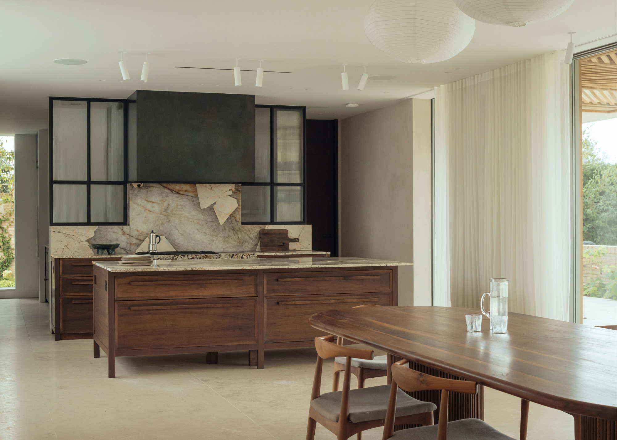 A sleek modern dark wood kitchen with light stone surfaces and glass partitions