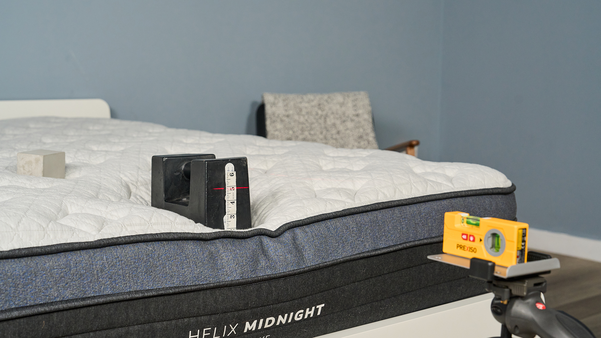 A close up of a 25kg weight balanced on the edge of the Helix Midnight Luxe mattress in our sleep studio. A laser is pointed at the side of the weight where a tape measure is placed.
