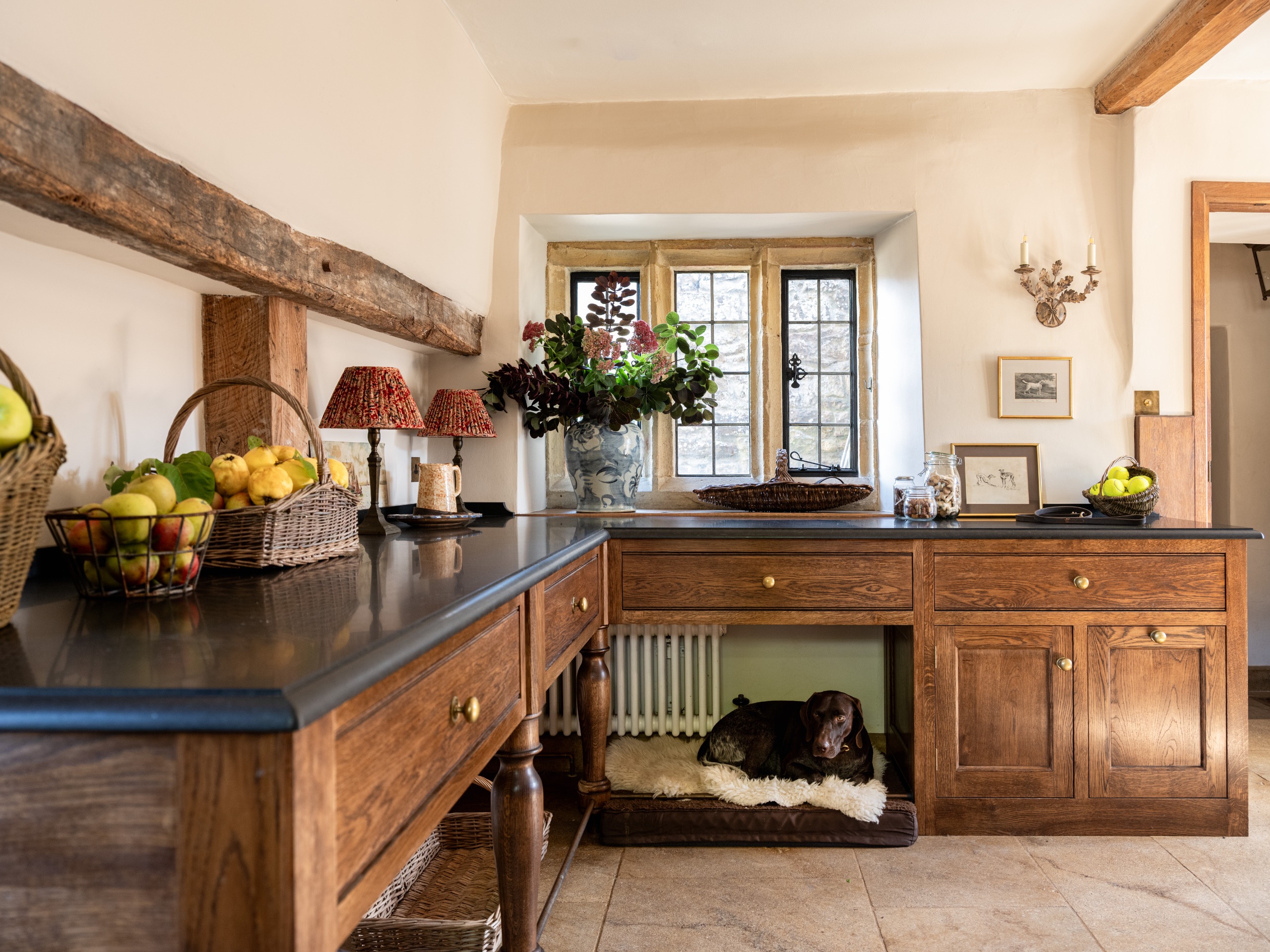 A dog sits on its bed underneath a dark wood countertop