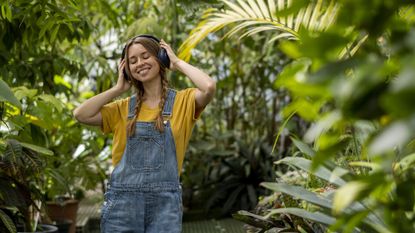 A smiling woman listens to headphones among plants