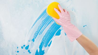 A window being cleaned with a sponge held by a pink rubber gloved hand