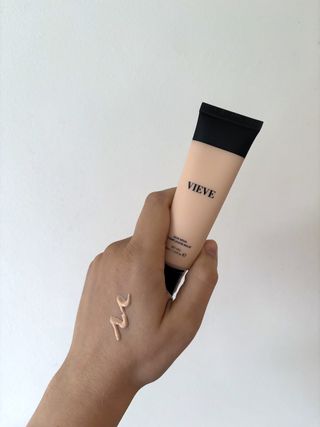 Mica Ricketts holding tube of Vieve Skin Nova Complexion Balm with swatch of product on hand