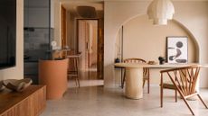 A living room with beige walls, an overhead fabric lamp light, a cream table with a pair of wood armchairs