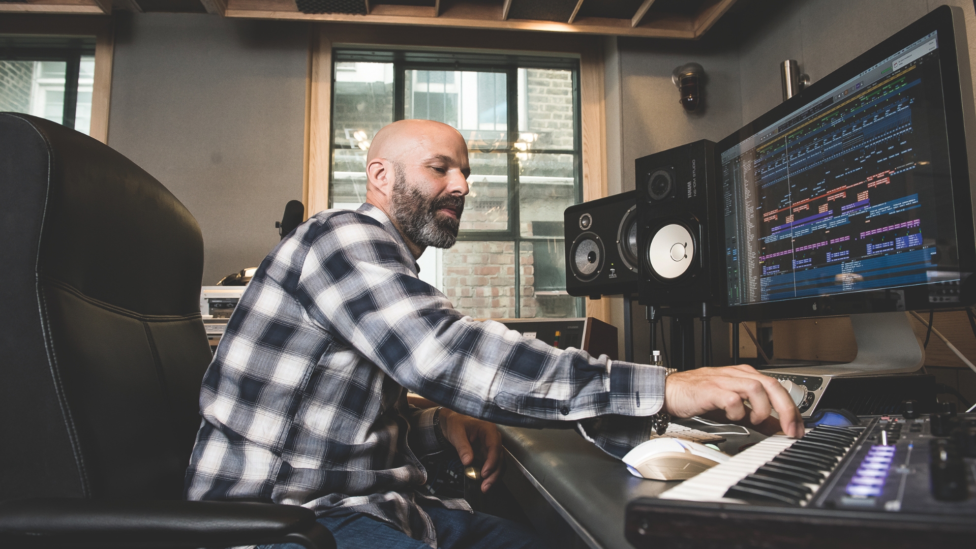 A man plays a MIDI keyboard in a recording studio