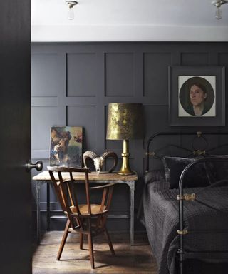 A black metal bedframe in a deep blue room besdies a wooden desk and chair