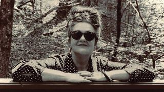 Holly Golightly in sunglasses, leaning on a fence