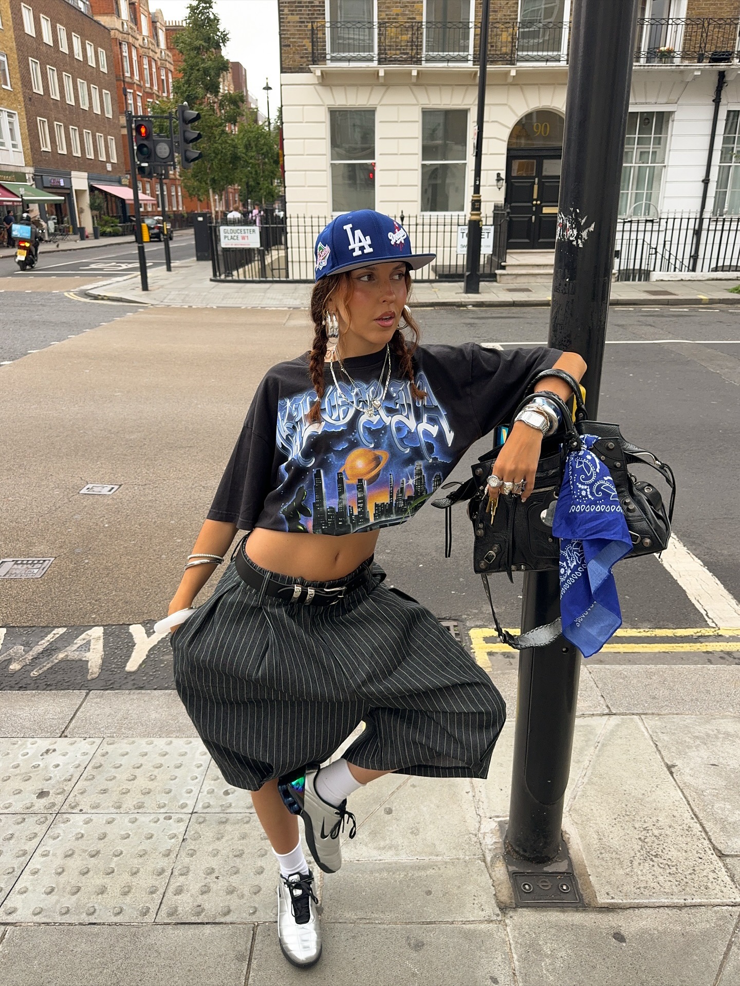 A woman wears metallic sneakers(one of the biggest sneaker color trends of 2026), stripe bermuda shorts, a cropped t-shirt, and a blue LA hat.