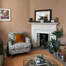 Plaster pink living room with a grey and white patterned armchair, white picture rail and moss green sofa.