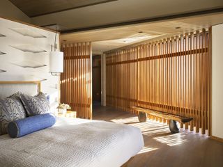 A white bed with blue scatter cushions in a bedroom with wooden panelling