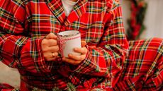 Someone wearing tartan Christmas pyjamas while holding a cup