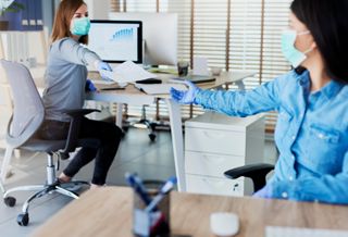 Women exchanging papers at work while maintaining social distancing