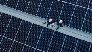 Two technicians stood on top of a roof covered in solar panels, to represent green data centers and renewable energy.