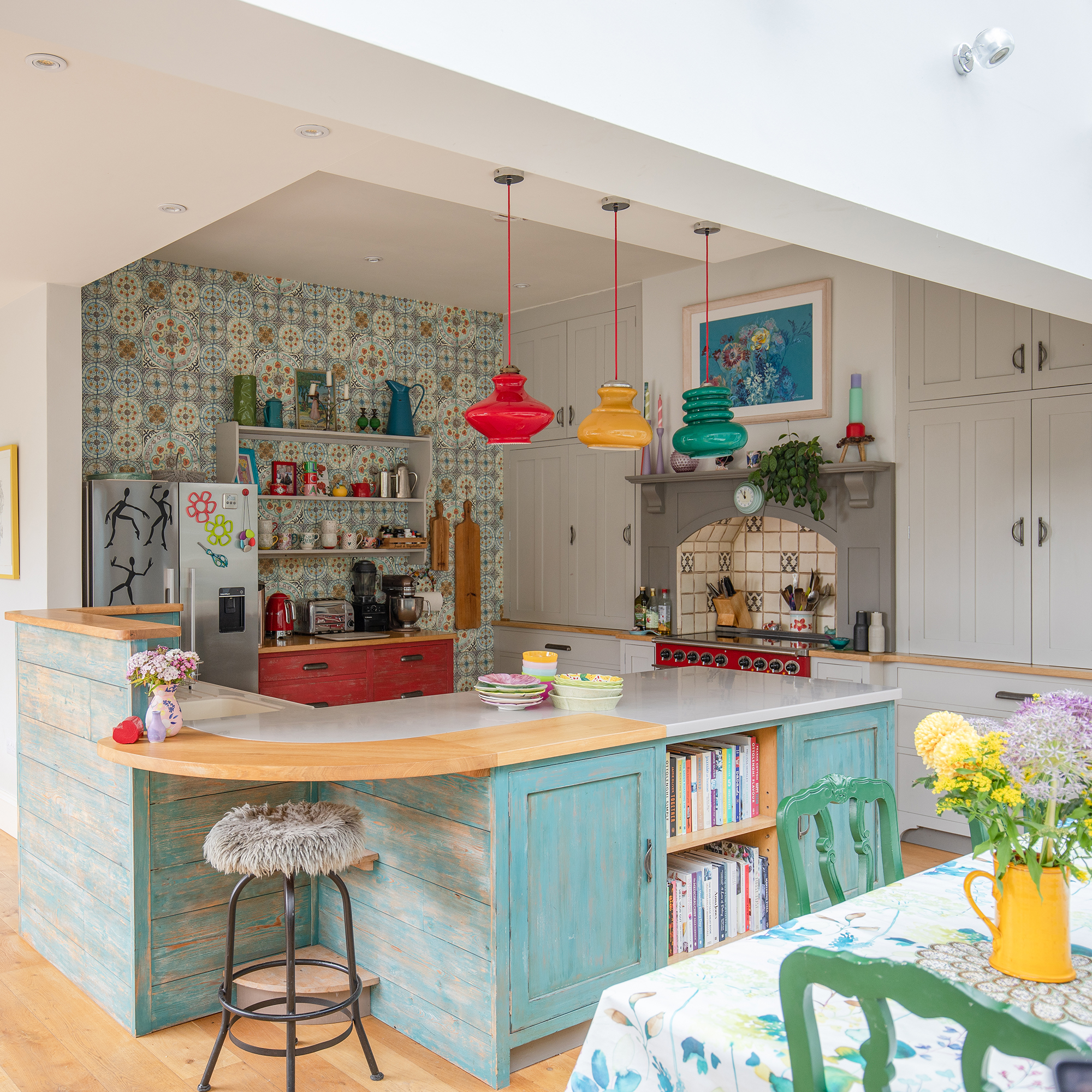 Colourful open-plan kitchen diner with a curved island and colourful glass pendant lights above