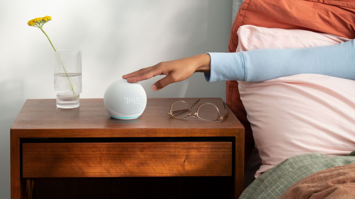 Hand reaching out towards Amazon Echo Dot with Clock on a bedside cabinet 