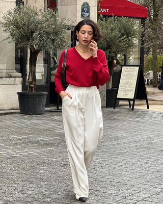 French influencer wearing white tailored trousers, red jumper and black shoulder bag.