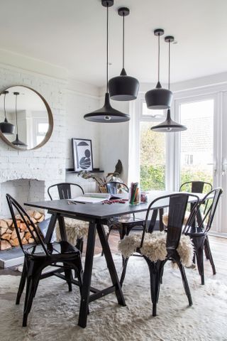 Pendant light ideas: monochrome dining room with black table and metal chairs, a mix of black pendant lights at various heights, a white-painted brick wall and a white hide rug beneath