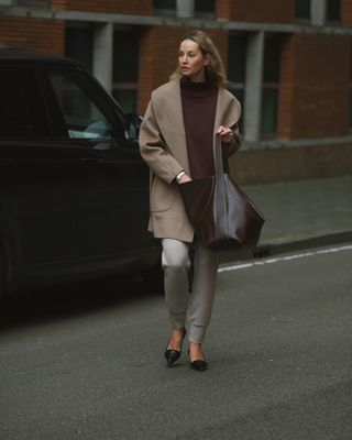 Anouk Yve in a burgundy sweater, brown tote bag, and kitten heels.