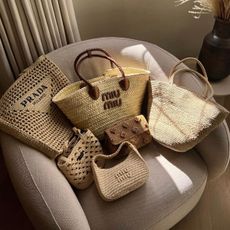 A selection of designer basket bags sit on top of a pink armchair