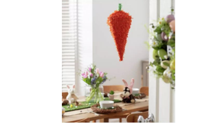 A carrot-shaped pinata hanging in a stylish kitchen above a table dressed for an Easter celebration