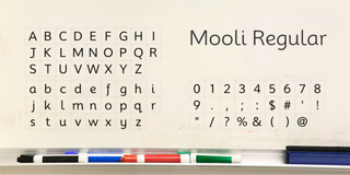 Mooli Regular font superimposed on school whiteboard, showing alphabet and numbers with typical symbols