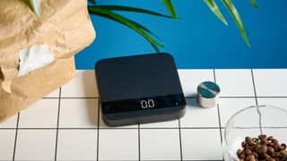 the acaia lunar coffee scale in black with an aluminum surface and accurate precise weight ideal for espresso machines given its compact size is photographed againt a blue tom's guide background