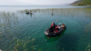 We see an inflatable black boat with researchers in it near the coast of a lake.