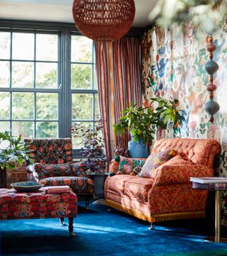 bright maximilist living room with bold patterned furniture, blue carpet, blue painted window frames, stripe drapes, bold wallpaper