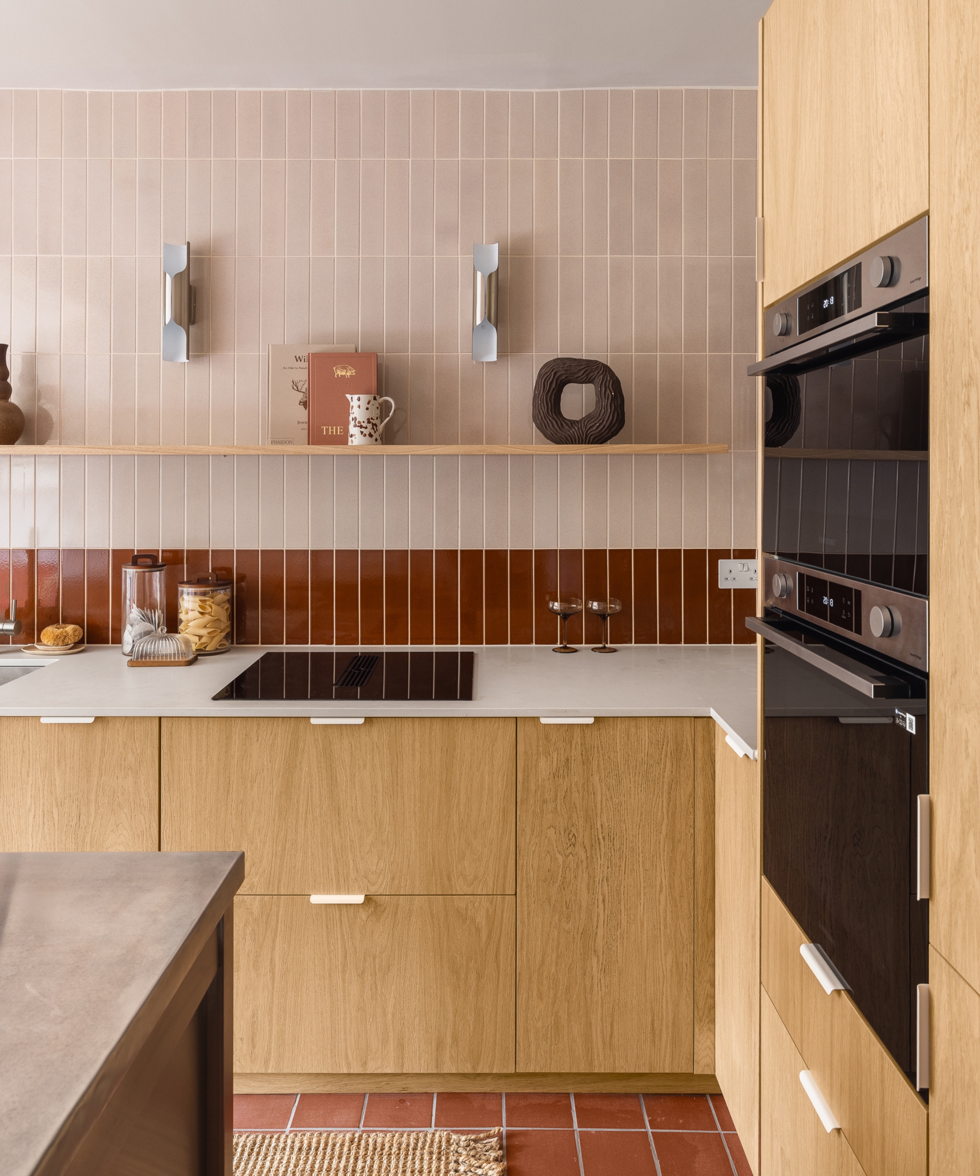 A small kitchen with cabinets made from pre-veneered MDF boards cut to project size, accompanied by a red and pink tiles backsplash and white countertops