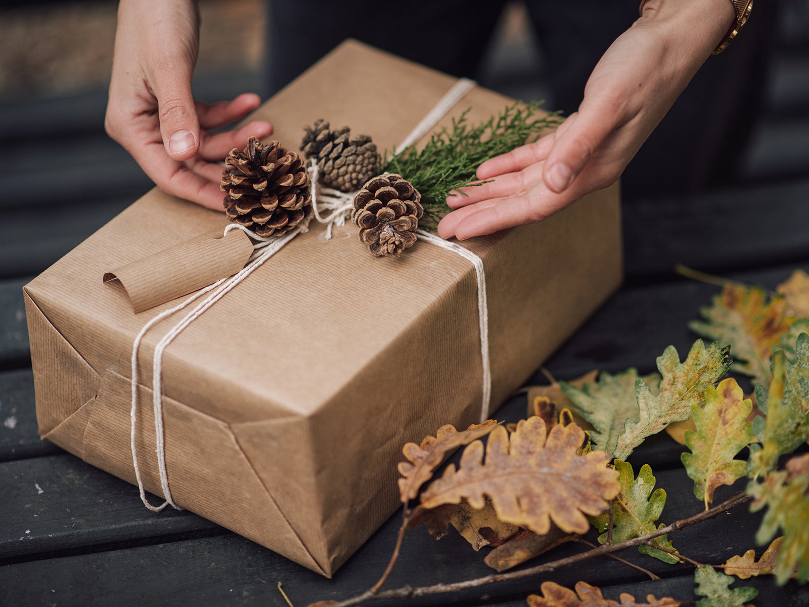 Decorated gift box. Natural colors, evergreen branches, and pine cones. Hands decorating gift box.