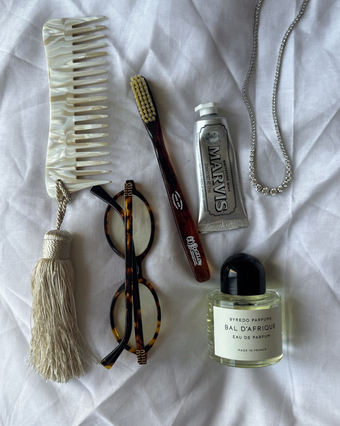 Miu Miu glasses on a sheet next to marble comb, brush, perfume bottle, and toothpaste.